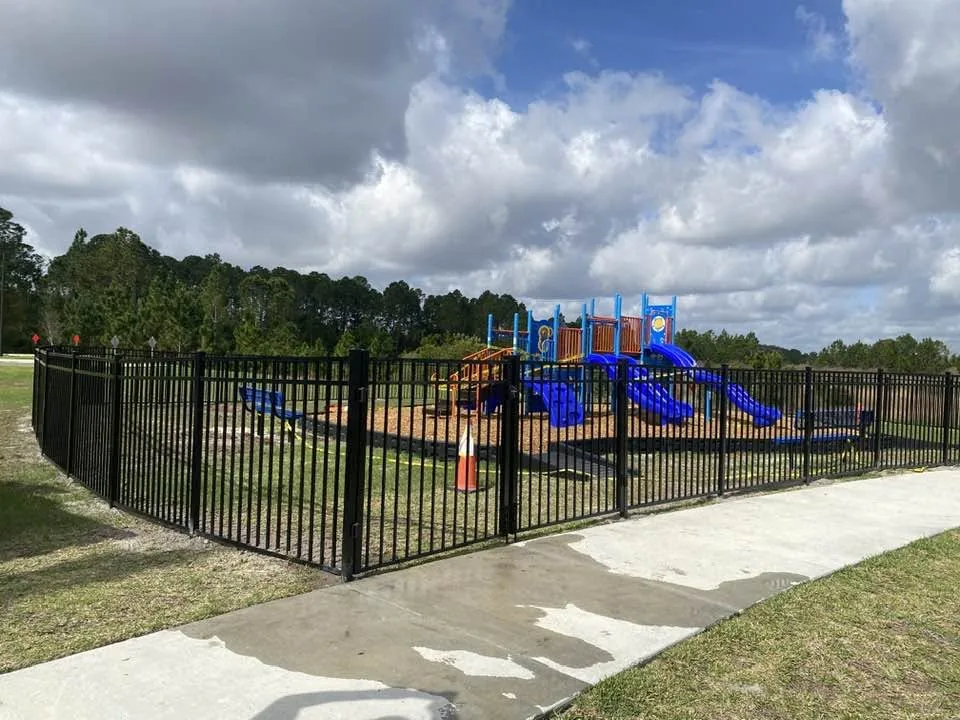 Black metal picket fence and gate surrounding a playground.