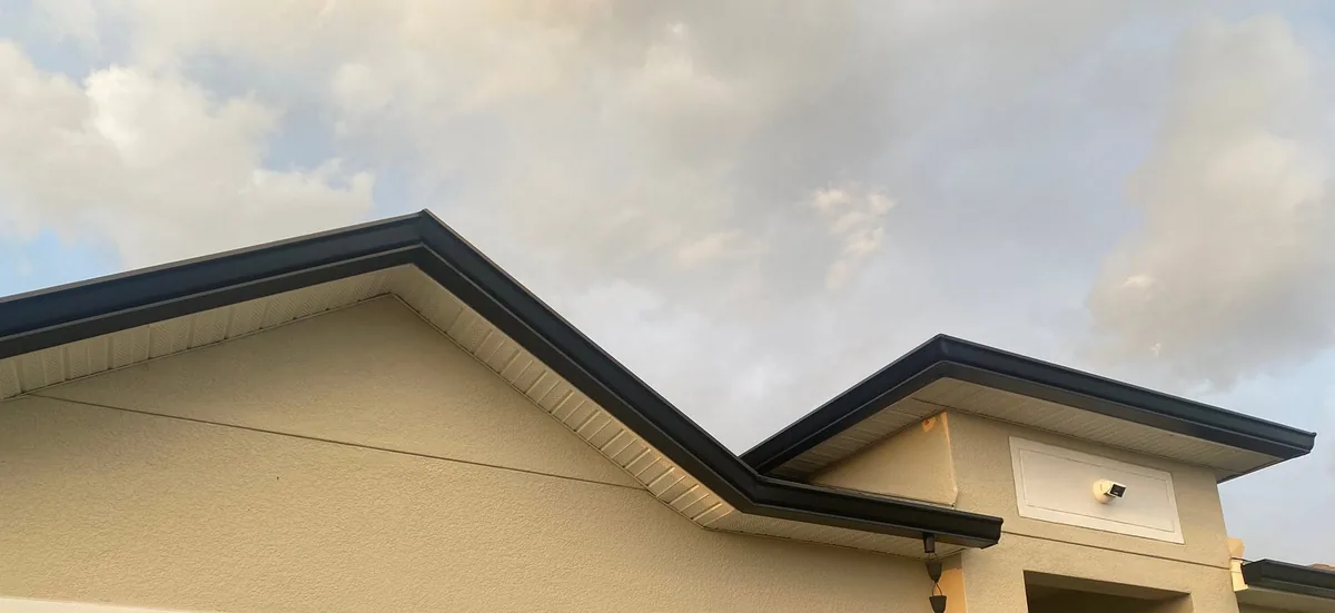 Canaletas oscuras a lo largo de los bordes de una fachada beige con frontones.