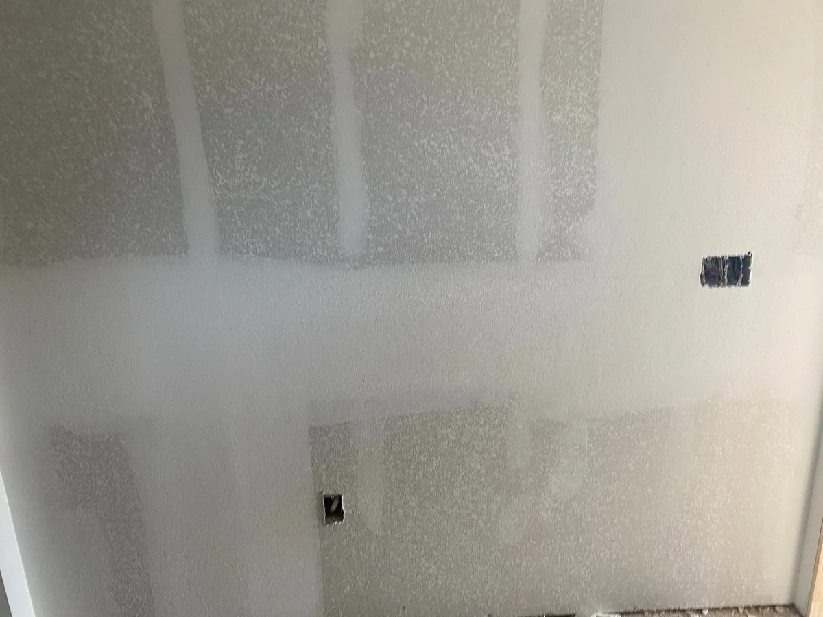 Drywall wall with joint compound covering seams and fastener points.