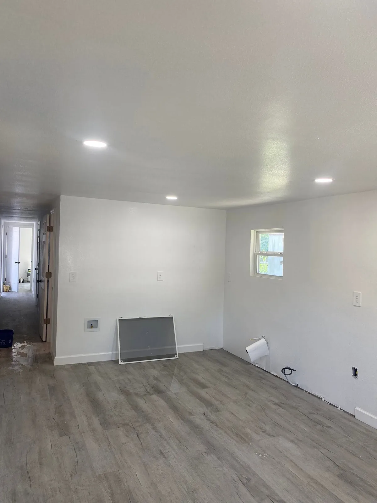 Habitación con paredes blancas, luces empotradas en el techo y piso gris con apariencia de madera.