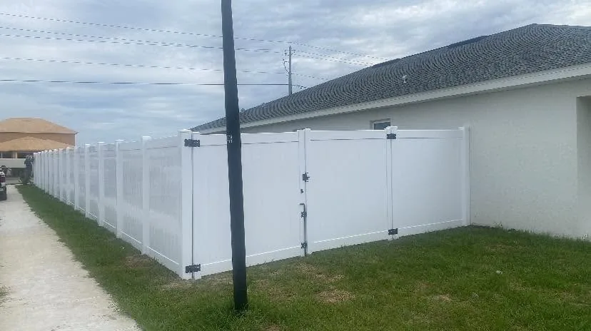 White privacy fence and a wide gate beside a light-colored house.