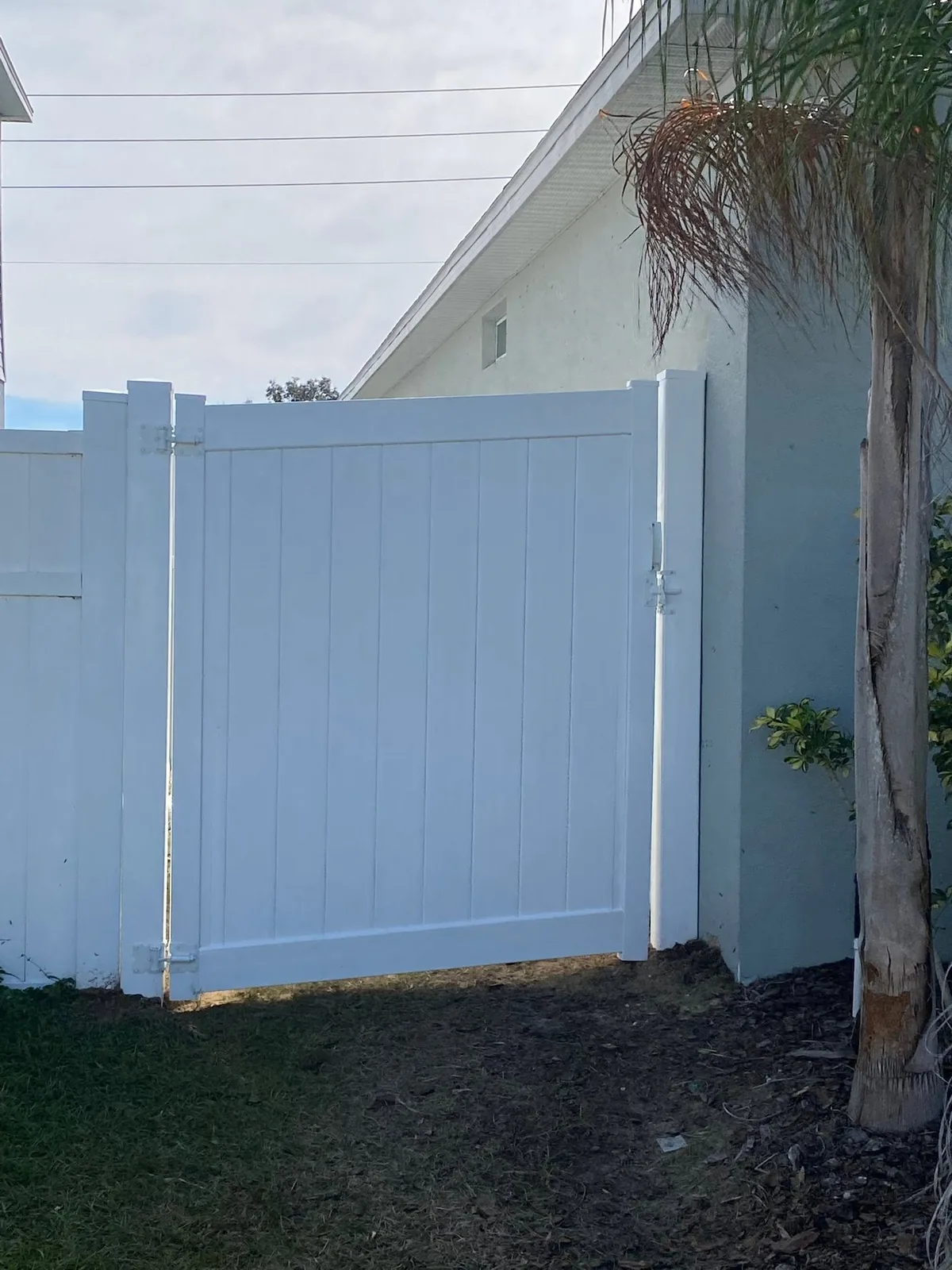 White vinyl gate between a house wall and a white fence.